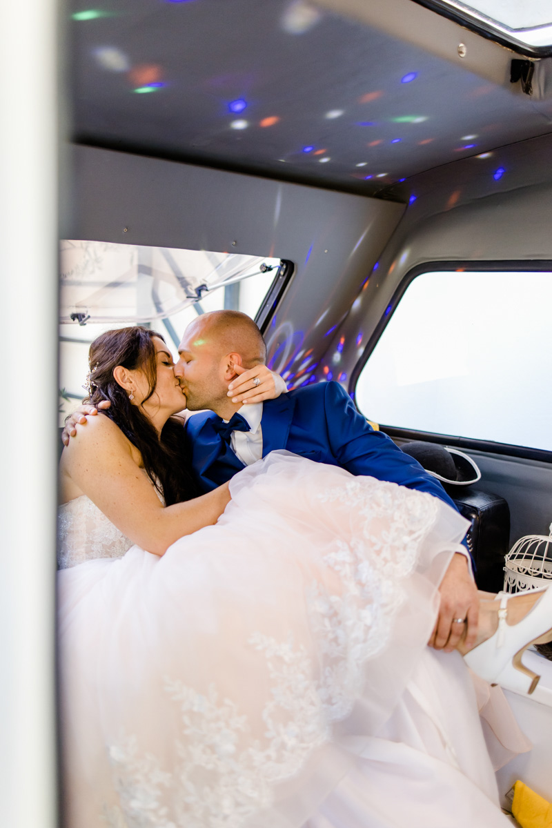 Wedding photo from the wedding photographer, sitting in the car on the back seat and kissing passionately, colourful lights all around :: photo copyright Karin Bergmann